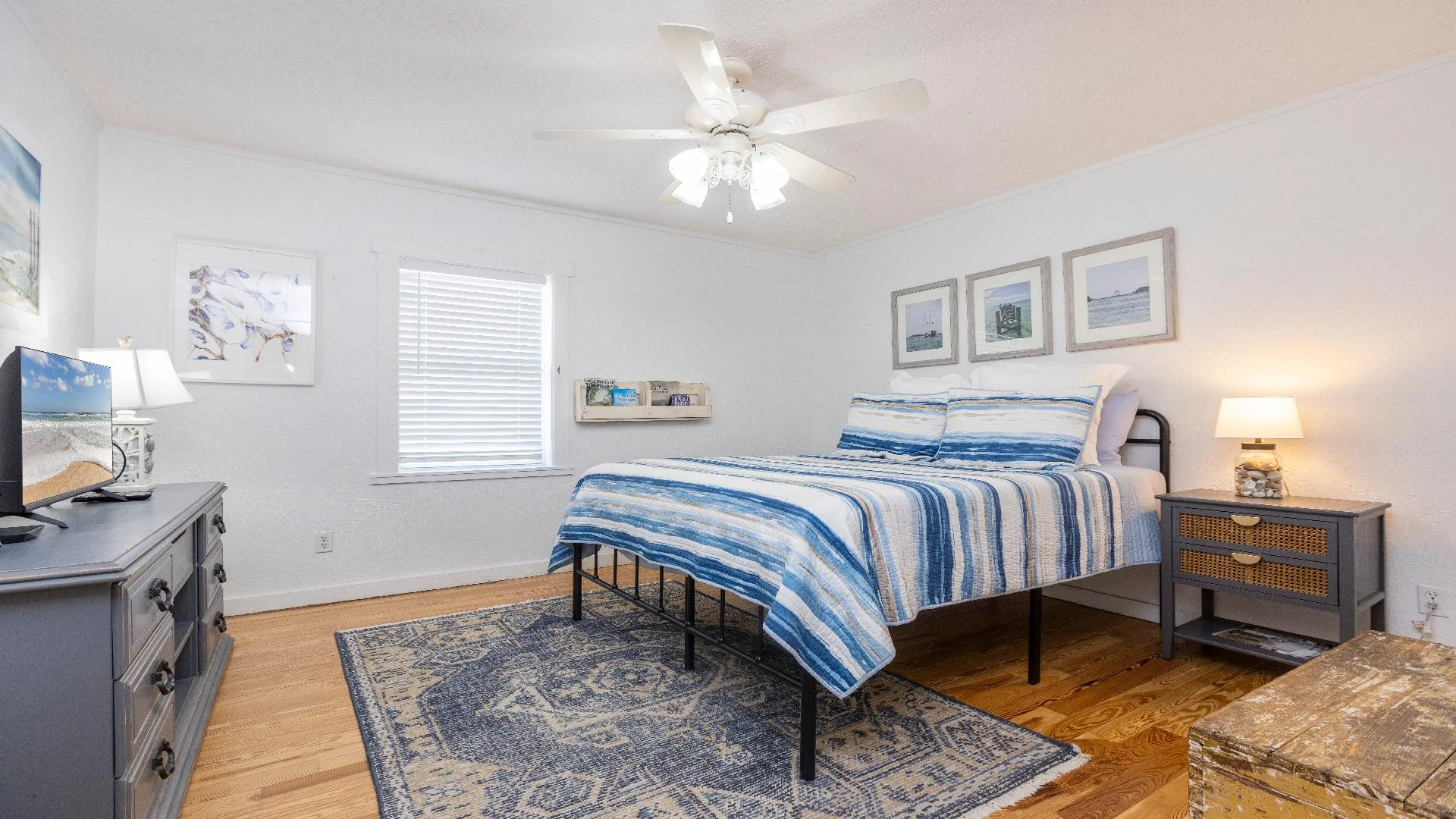 Bedroom with striped blue bedding on a black metal bed frame, gray dresser, patterned rug, and wood floors.
