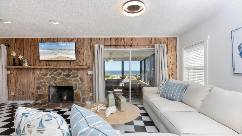 Living room with white sectional, round wood coffee table, stone fireplace, and sliding glass door to screened porch.