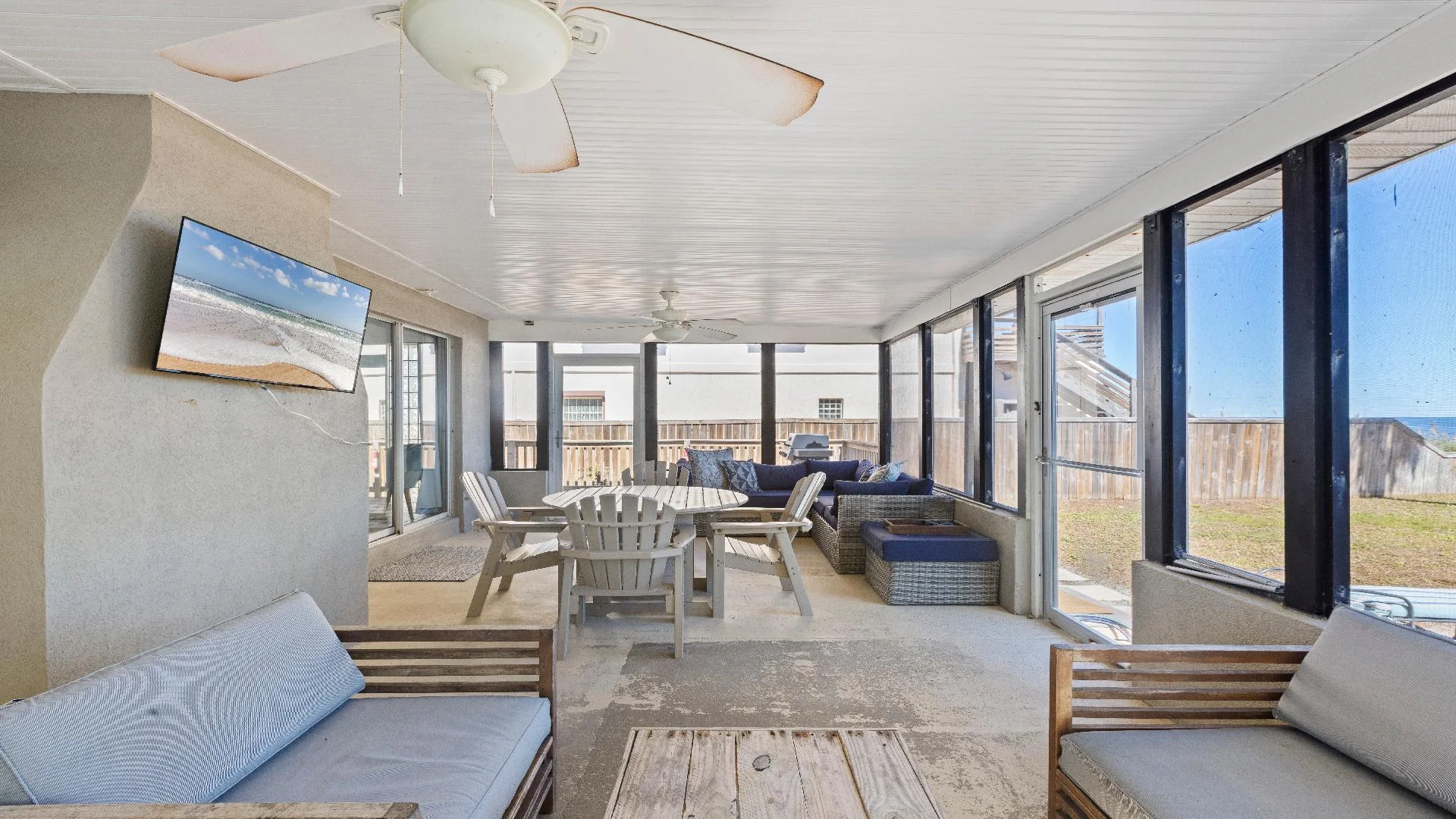 Screened porch with wooden Adirondack chairs around a round table, wicker sectional, ceiling fans, and ocean views.
