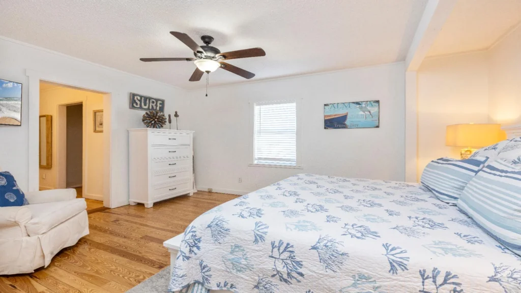 Bedroom with hardwood floors, white dresser, ceiling fan, and coastal-themed bedding and artwork.