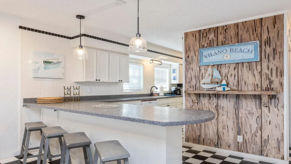 Speckled gray countertop extends from white cabinetry with black hardware, accented by glass pendant lights.