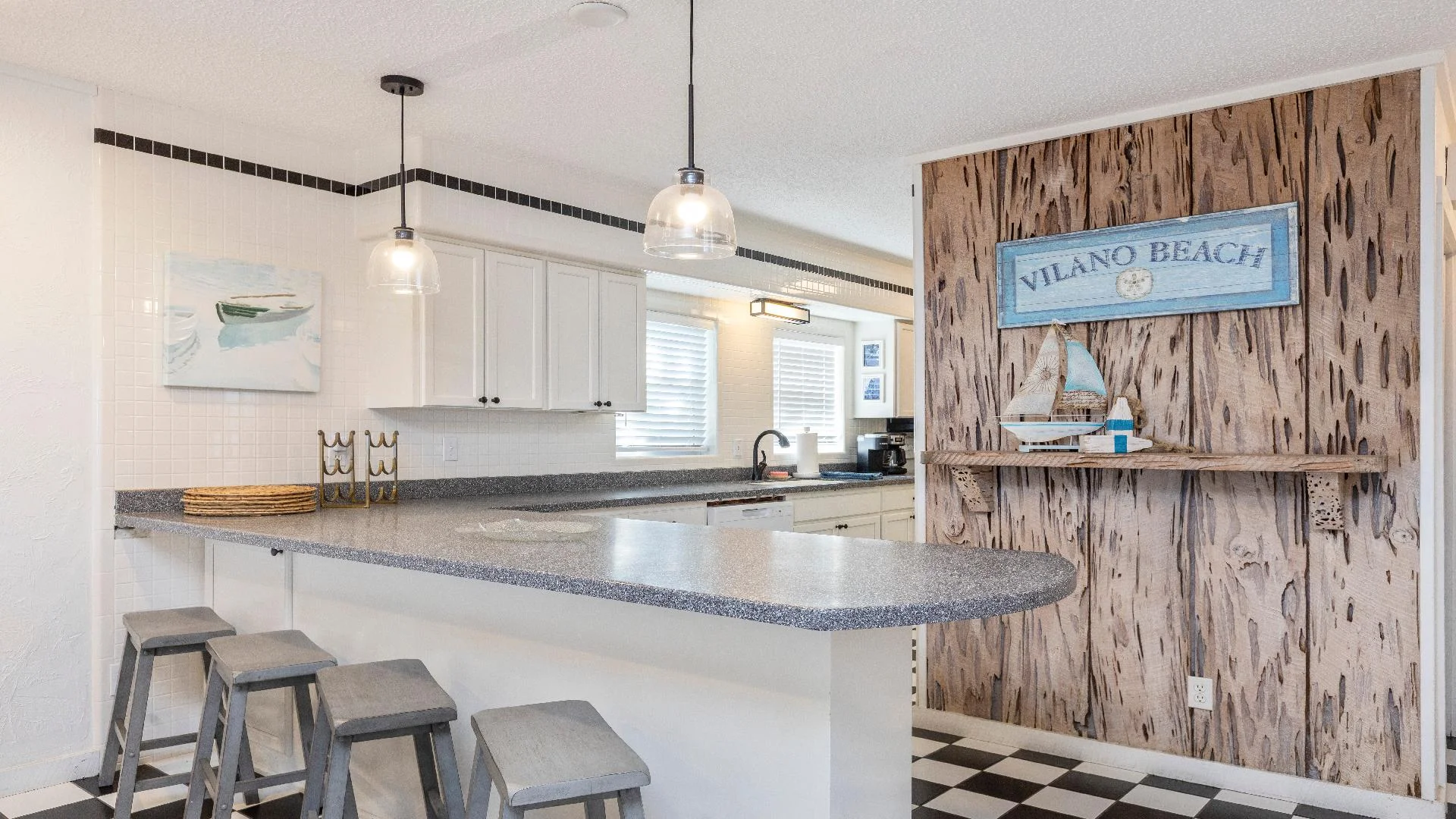 Speckled gray countertop extends from white cabinetry with black hardware, accented by glass pendant lights.