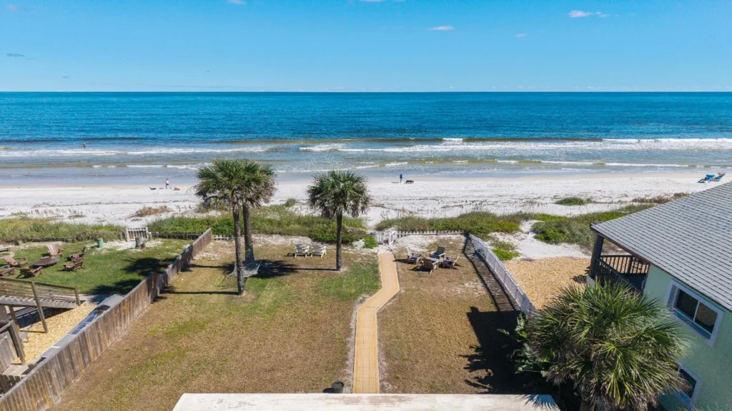 Oceanfront backyard with palm trees, a paved walkway, Adirondack chairs, and direct beach access.