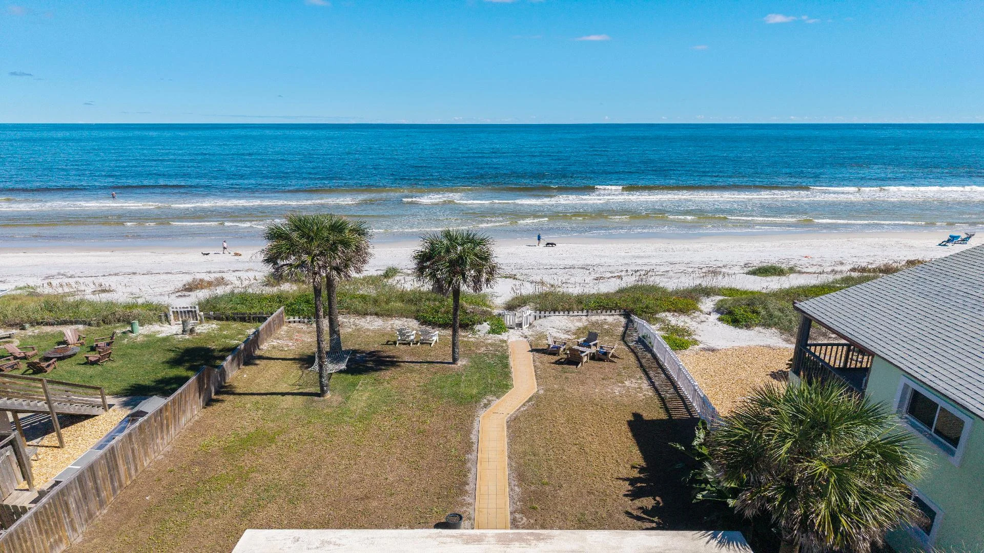 Oceanfront backyard with palm trees, a paved walkway, Adirondack chairs, and direct beach access.