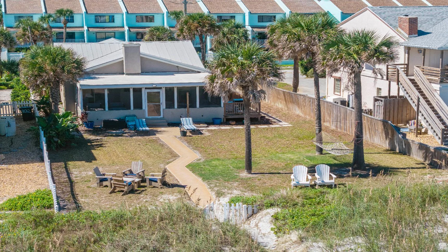 Oceanfront yard with palm trees, Adirondack chairs, hammock, and a sandy path leading to the beach.